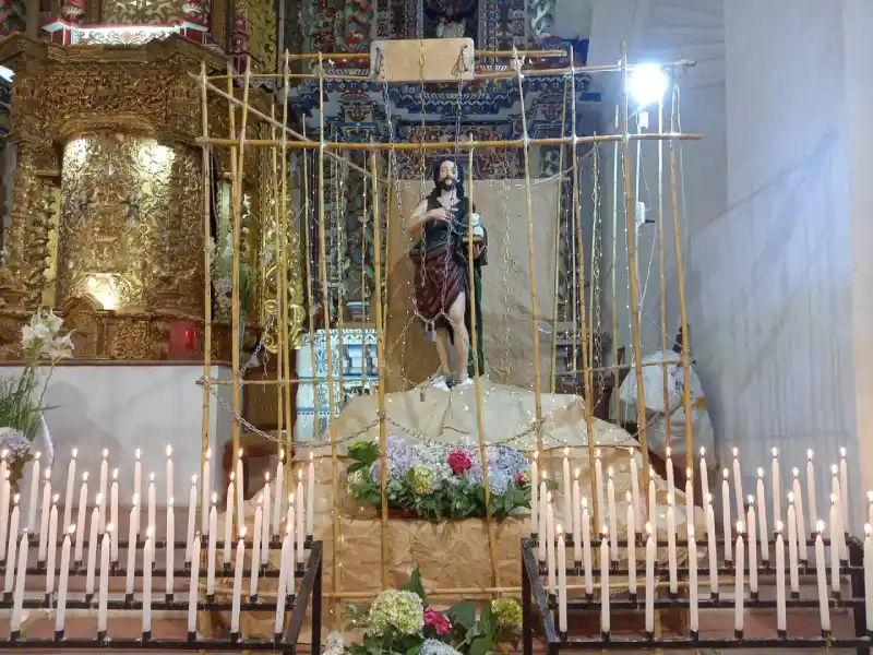 Imagen de San Juan Bautista en la iglesia de Pallasca rodeada de cirios encendidos durante la festividad patronal