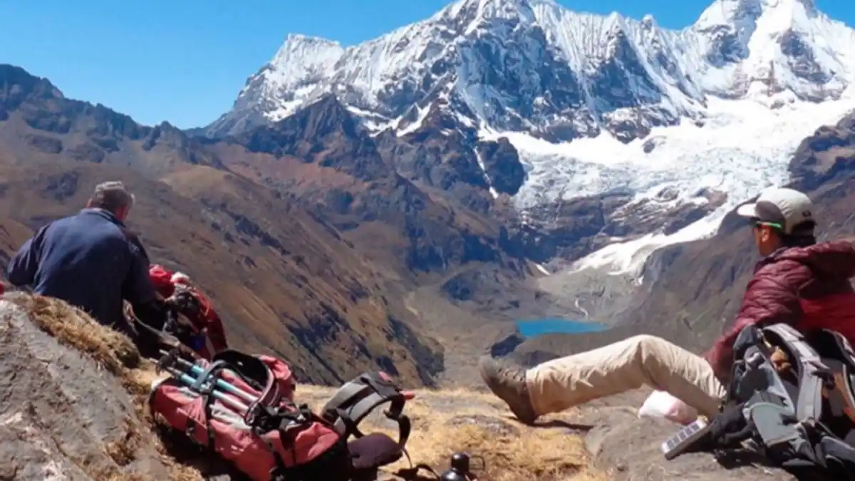 Dos turistas de aventura observan desde lo alto los nevados y una laguna en Áncash, destino clave del turismo de montaña en el Perú.